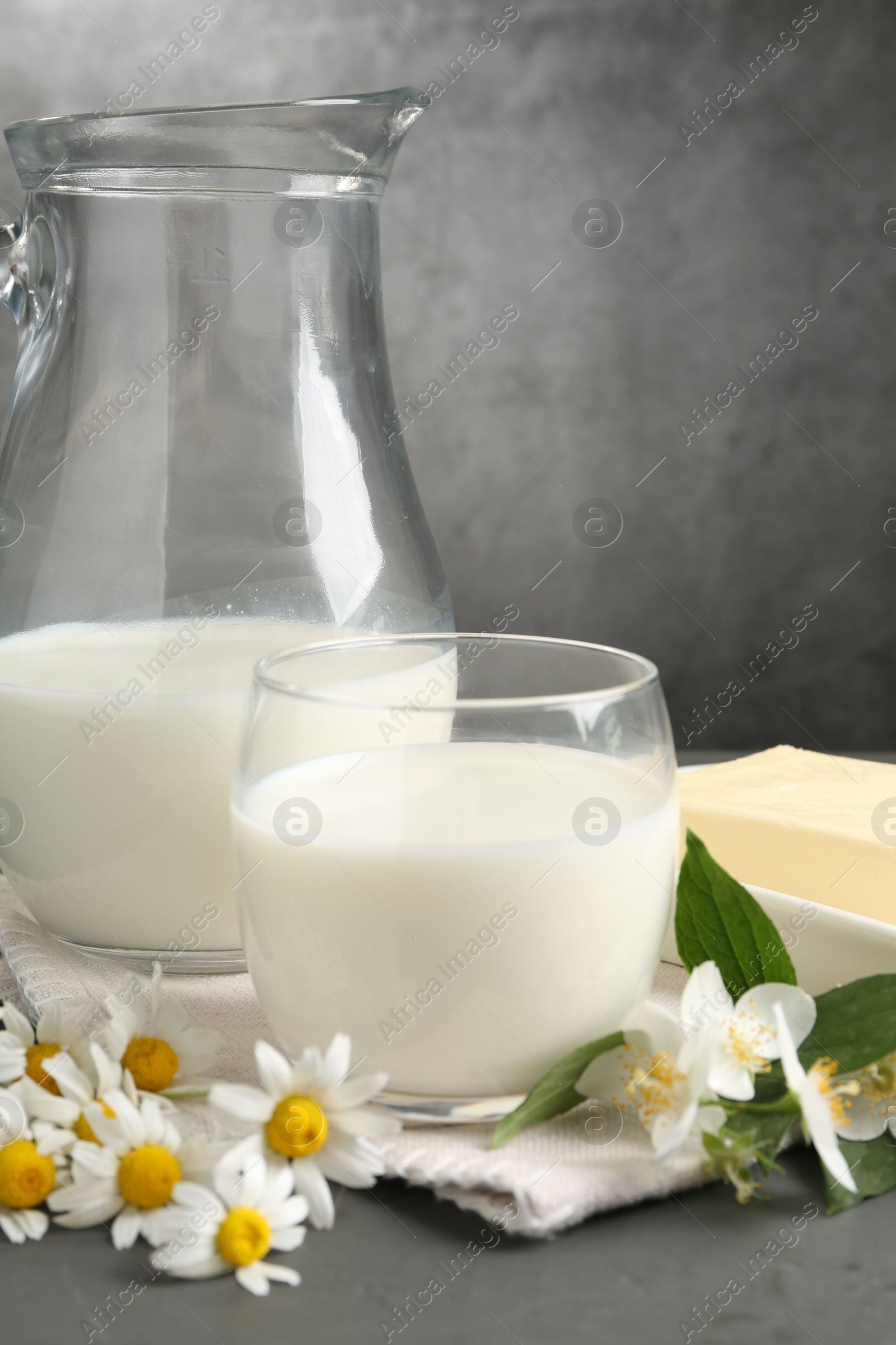 Photo of Fresh dairy products and flowers on grey wooden table against textured background, closeup
