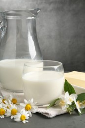 Photo of Fresh dairy products and flowers on grey wooden table against textured background, closeup
