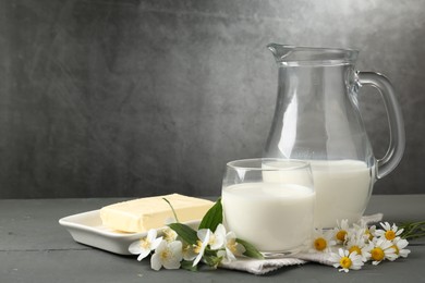 Photo of Fresh dairy products and flowers on grey wooden table against textured background. Space for text