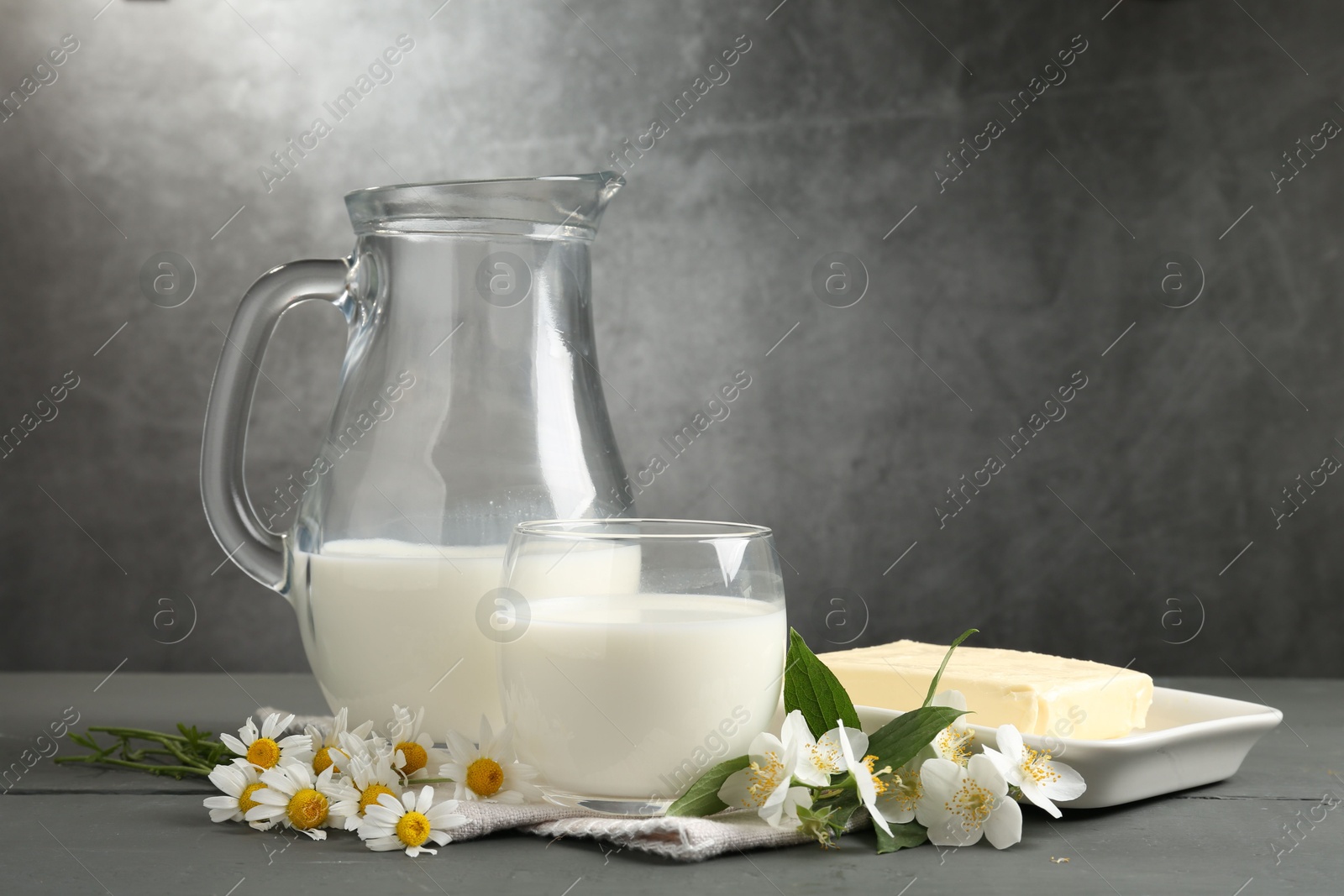 Fresh dairy products and flowers on grey wooden table against textured background Photo of Fresh dairy products and flowers on grey wooden table against textured background