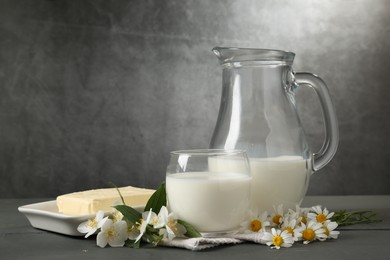 Photo of Fresh dairy products and flowers on grey wooden table against textured background