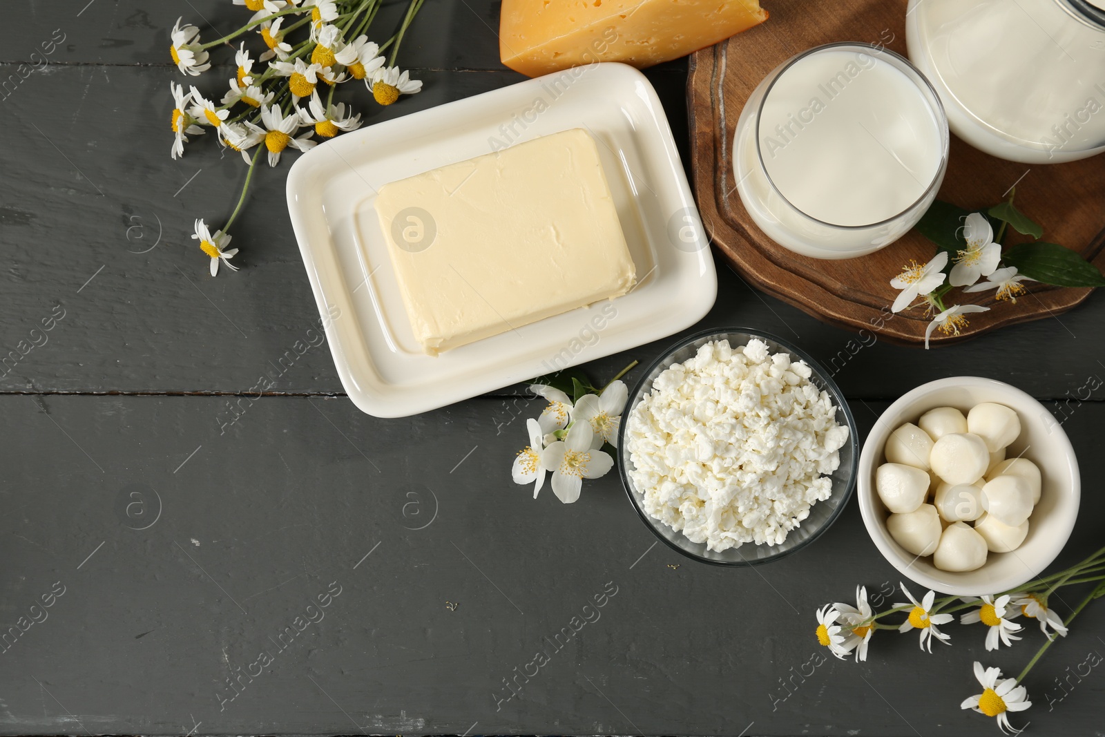 Photo of Fresh dairy products and flowers on grey wooden table, flat lay. Space for text