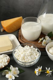 Photo of Fresh dairy products and flowers on grey wooden table against dark background