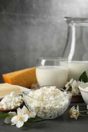 Photo of Fresh dairy products and flowers on grey wooden table against textured background, closeup