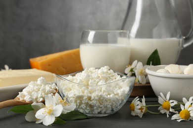 Photo of Fresh dairy products and flowers on grey wooden table against textured background, closeup
