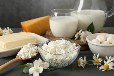 Photo of Fresh dairy products and flowers on grey wooden table against textured background, closeup