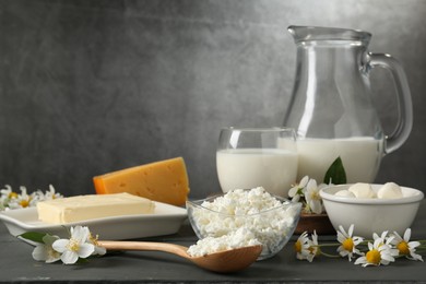 Photo of Fresh dairy products and flowers on grey wooden table against textured background