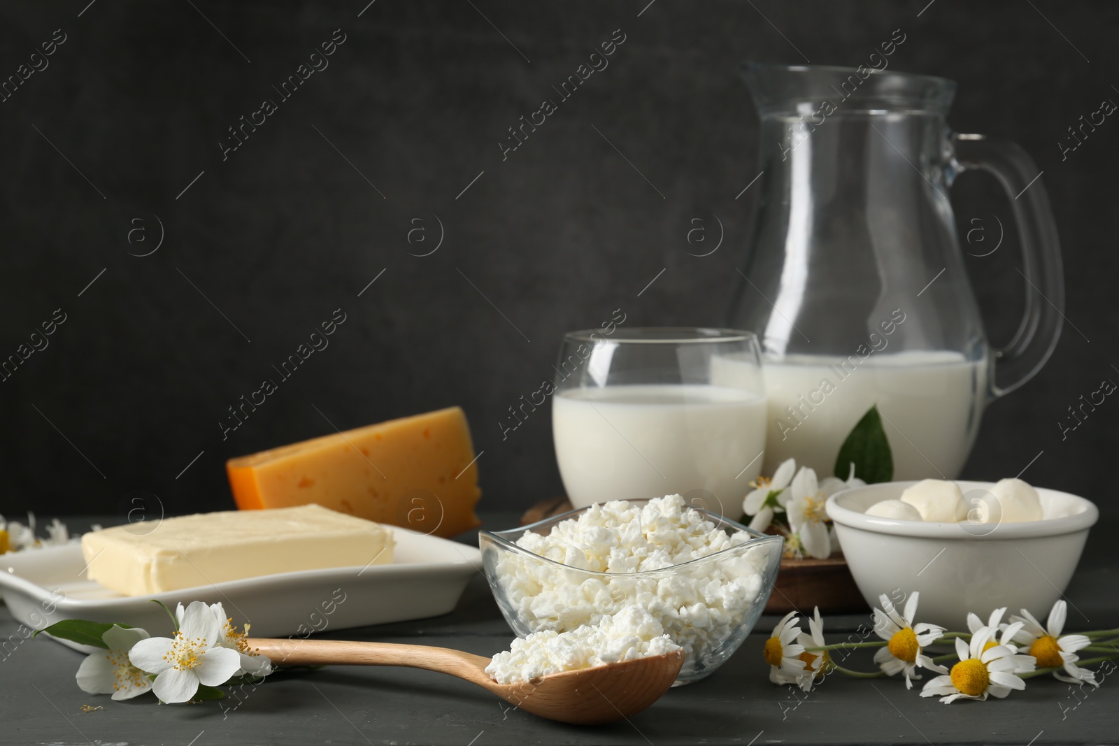 Photo of Fresh dairy products and flowers on grey wooden table against dark background