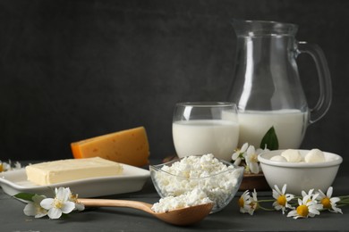 Photo of Fresh dairy products and flowers on grey wooden table against dark background
