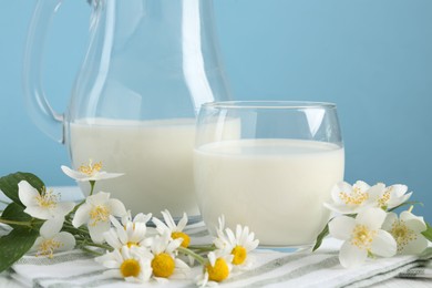 Photo of Fresh milk and flowers on table against light blue background, closeup. Dairy product