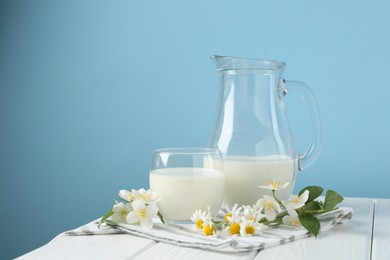 Photo of Fresh milk and flowers on white wooden table against light blue background. Dairy product