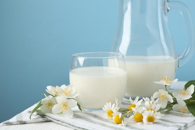 Photo of Fresh milk and flowers on white wooden table against light blue background, closeup. Dairy product