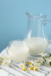Photo of Fresh milk and flowers on white wooden table against light blue background, closeup. Dairy product