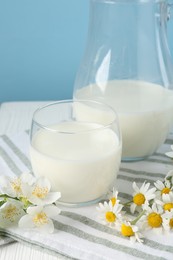 Photo of Fresh milk and flowers on white wooden table against light blue background, closeup. Dairy product