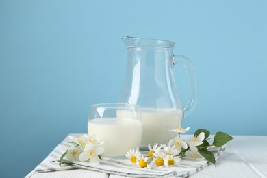 Photo of Fresh milk and flowers on white wooden table against light blue background. Dairy product