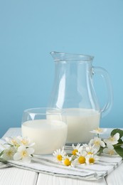 Photo of Fresh milk and flowers on white wooden table against light blue background. Dairy product