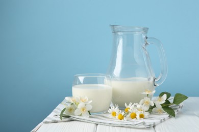 Photo of Fresh milk and flowers on white wooden table against light blue background, space for text. Dairy product