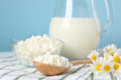 Photo of Fresh cottage cheese, milk and chamomile flowers on table against light blue background, closeup. Dairy products