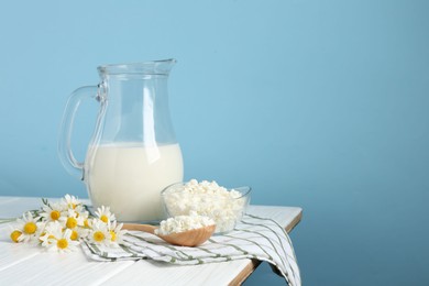 Photo of Fresh milk in jug, cottage cheese and chamomile flowers on white wooden table against light blue background, space for text. Dairy products