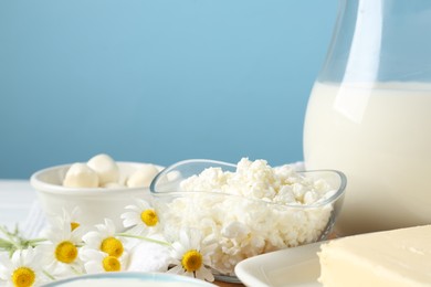 Photo of Fresh dairy products and flowers on table against light blue background, closeup