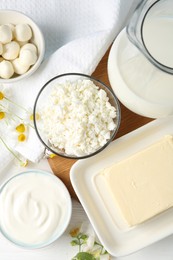 Photo of Fresh dairy products and flowers on white wooden table, flat lay