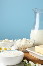 Photo of Fresh dairy products and flowers on white wooden table against light blue background, closeup