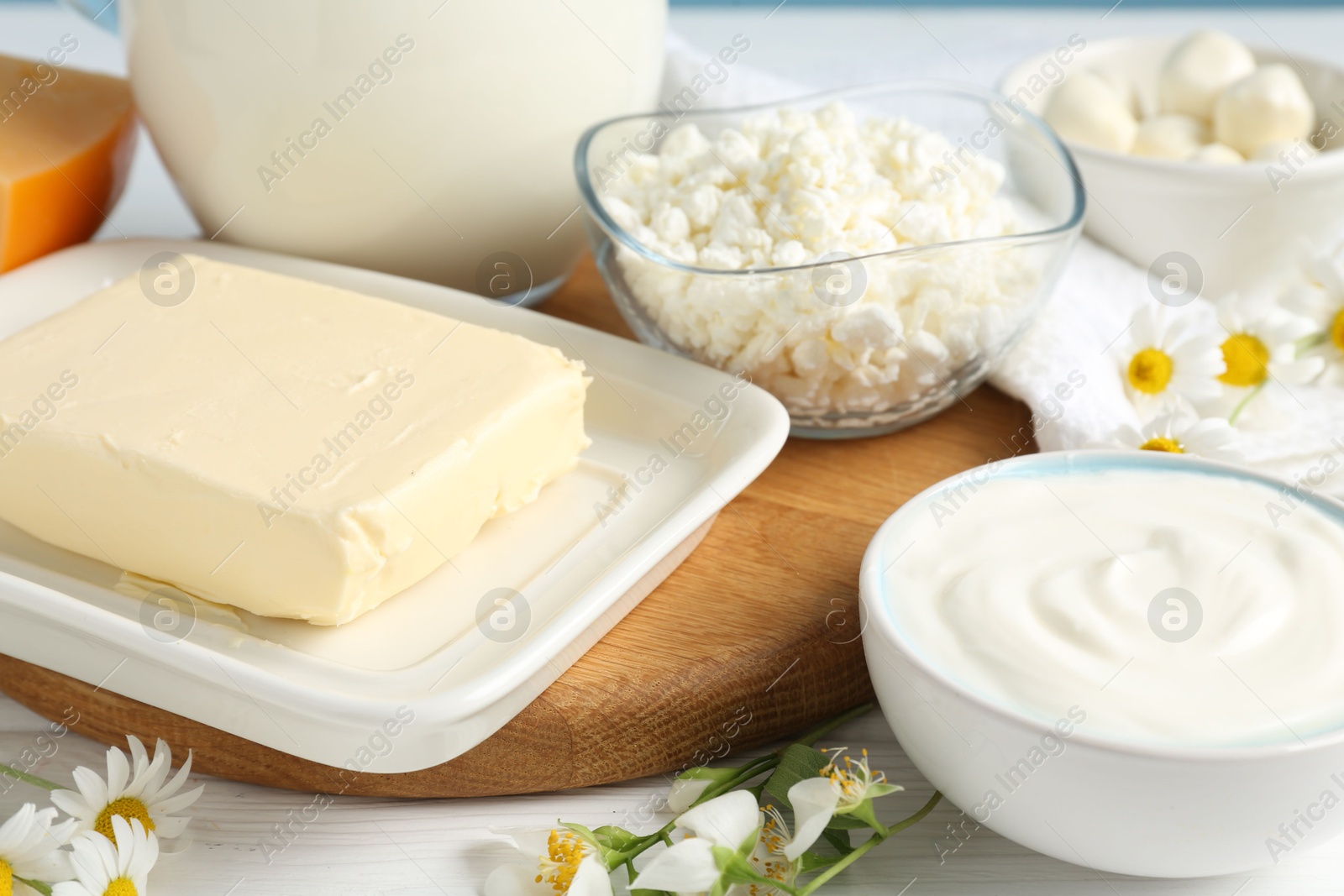 Photo of Fresh dairy products and flowers on white wooden table, closeup