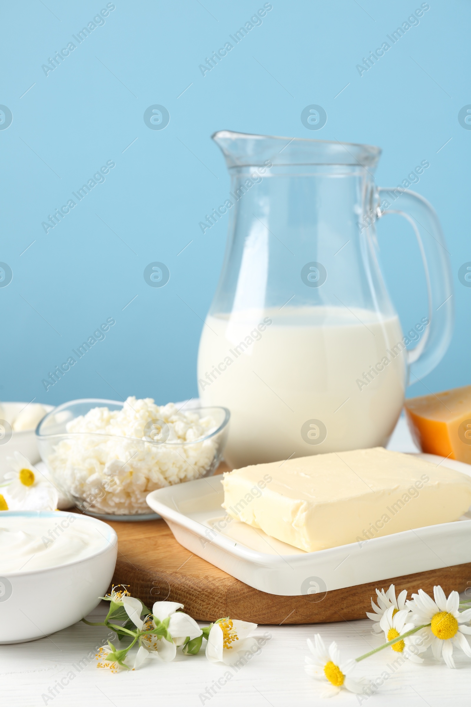 Fresh dairy products and flowers on white wooden table against light blue background, closeup Photo of Fresh dairy products and flowers on white wooden table against light blue background, closeup