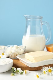 Photo of Fresh dairy products and flowers on white wooden table against light blue background, closeup