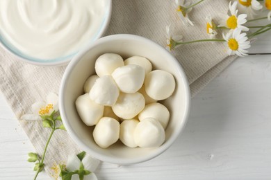 Photo of Fresh mozzarella cheese, sour cream in bowls and flowers on white wooden table, flat lay. Dairy products