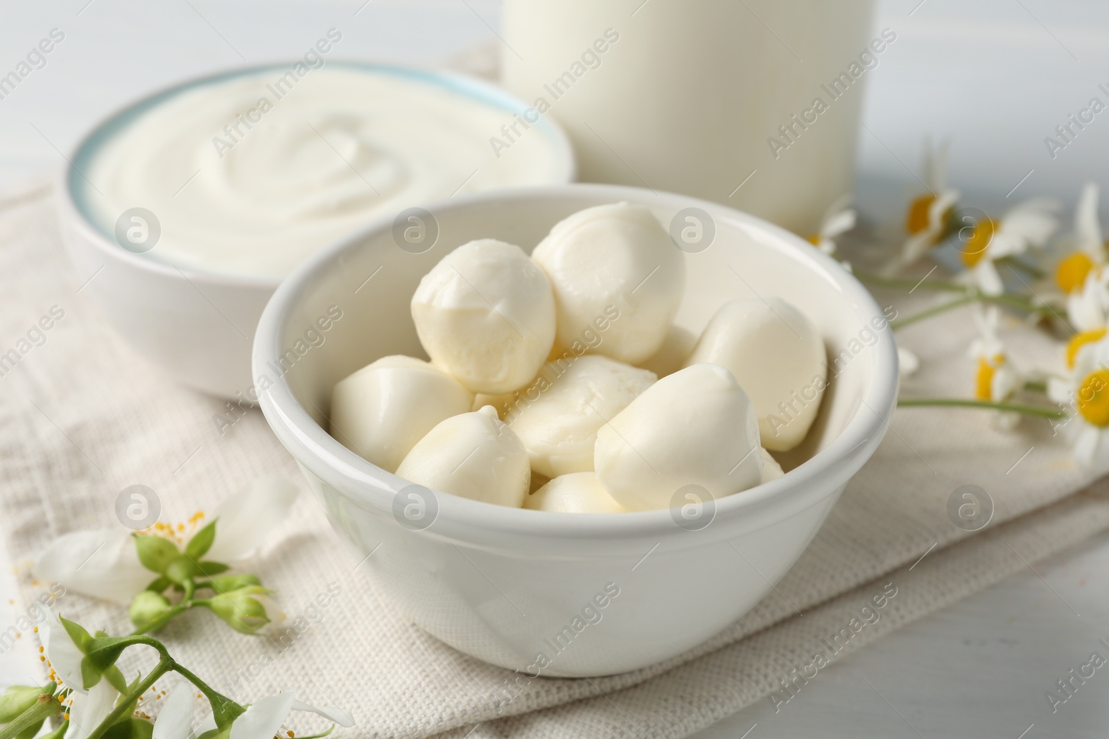 Photo of Fresh mozzarella cheese, sour cream, milk and flowers on white wooden table, closeup. Dairy products