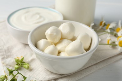 Photo of Fresh mozzarella cheese, sour cream, milk and flowers on white wooden table, closeup. Dairy products