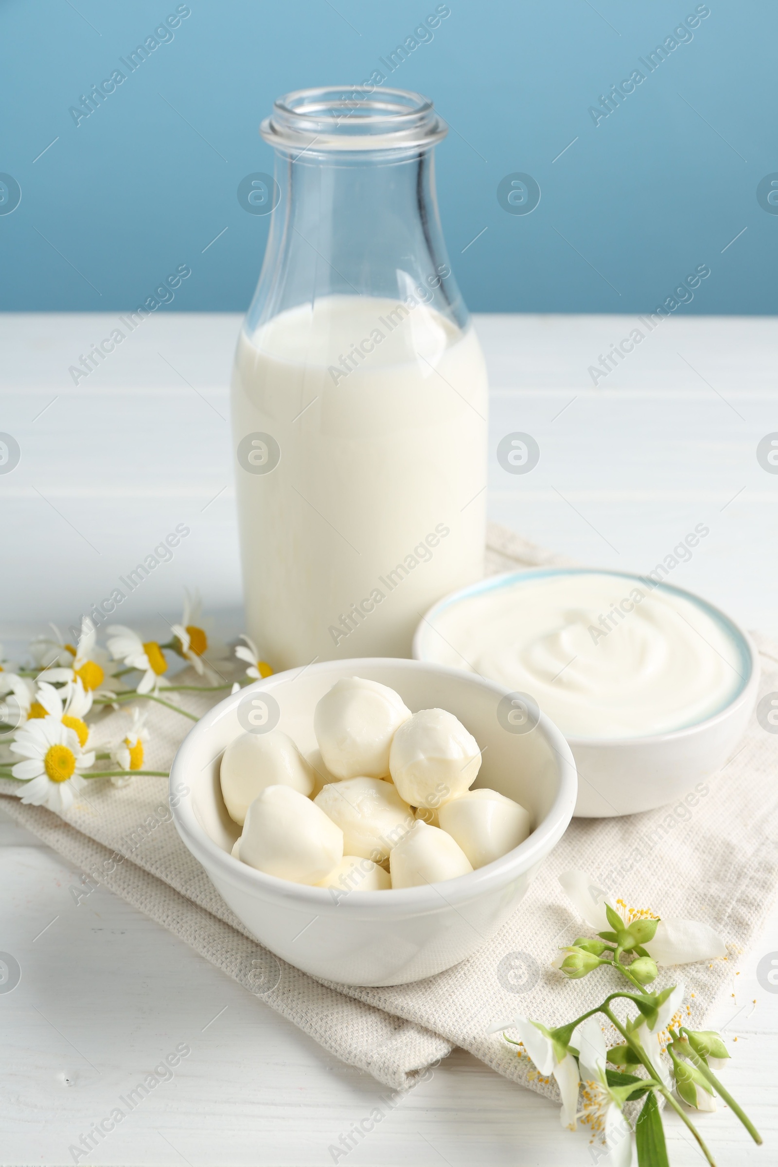 Fresh dairy products and flowers on white wooden table against light blue background Photo of Fresh dairy products and flowers on white wooden table against light blue background