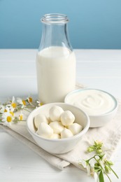 Photo of Fresh dairy products and flowers on white wooden table against light blue background