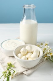 Photo of Fresh dairy products and flowers on white wooden table against light blue background