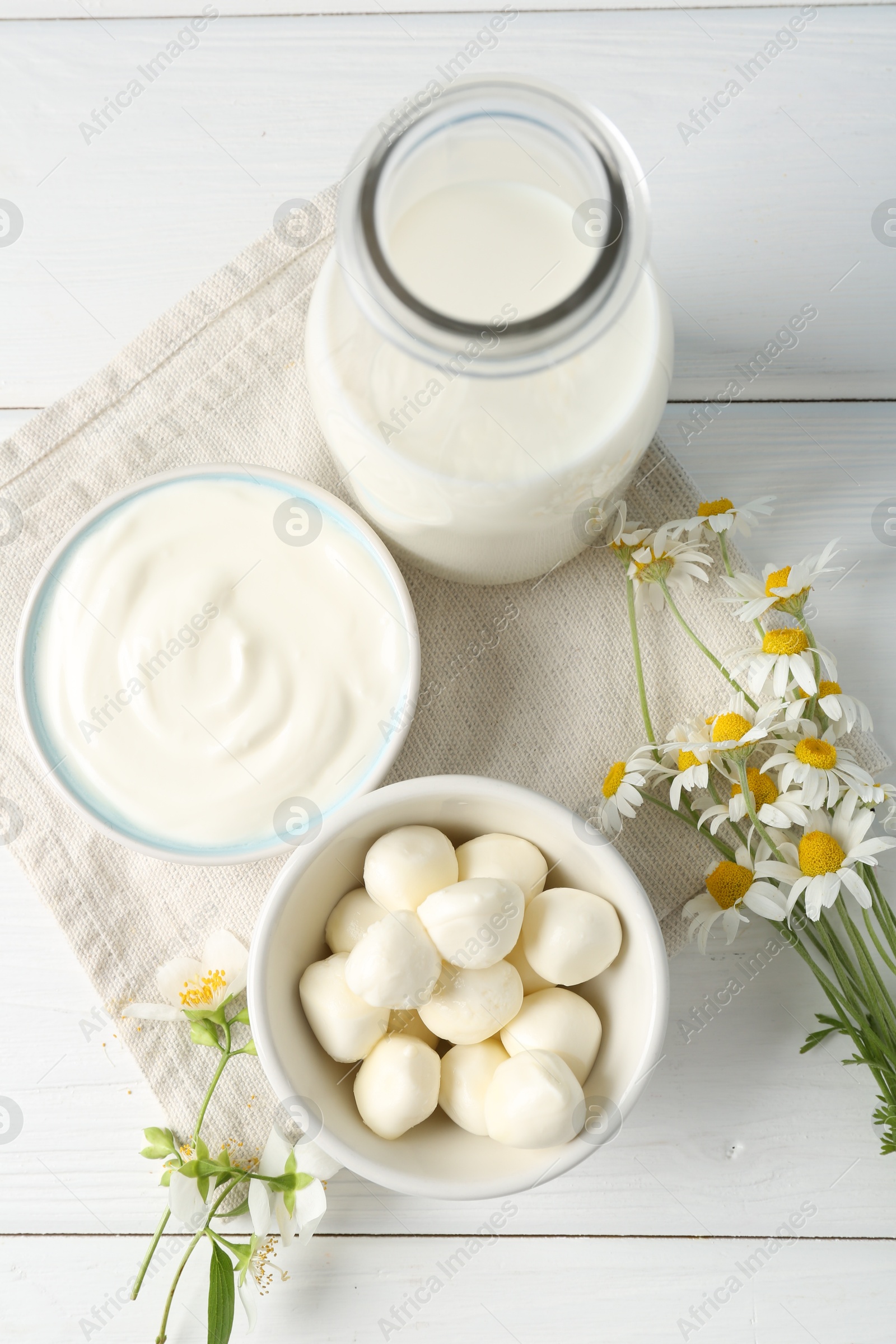 Photo of Fresh dairy products and flowers on white wooden table, flat lay