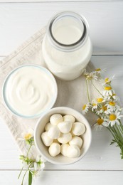 Photo of Fresh dairy products and flowers on white wooden table, flat lay