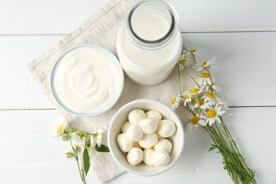 Photo of Fresh dairy products and flowers on white wooden table, flat lay