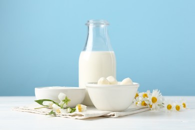 Photo of Fresh dairy products and flowers on white wooden table against light blue background