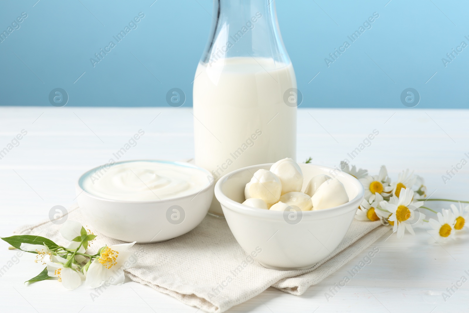 Fresh dairy products and flowers on white wooden table against light blue background, closeup Photo of Fresh dairy products and flowers on white wooden table against light blue background, closeup