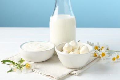 Photo of Fresh dairy products and flowers on white wooden table against light blue background, closeup