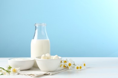 Photo of Fresh dairy products and flowers on white wooden table against light blue background. Space for text
