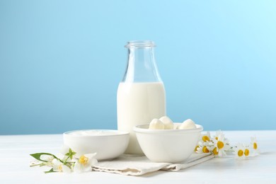 Photo of Fresh dairy products and flowers on white wooden table against light blue background