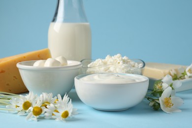 Photo of Fresh dairy products and flowers on light blue background, closeup