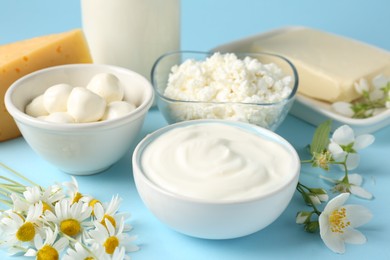 Photo of Fresh dairy products and flowers on light blue background, closeup