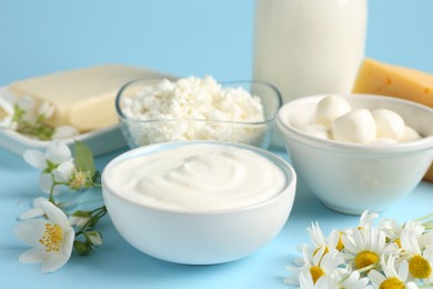Photo of Fresh dairy products and flowers on light blue background, closeup