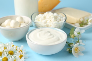Photo of Fresh dairy products and flowers on light blue background, closeup