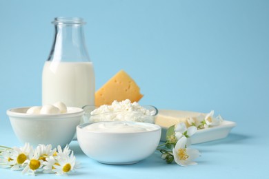 Photo of Fresh dairy products and flowers on light blue background, closeup