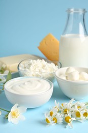 Photo of Fresh dairy products and flowers on light blue background, closeup