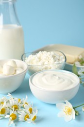 Photo of Fresh dairy products and flowers on light blue background, closeup